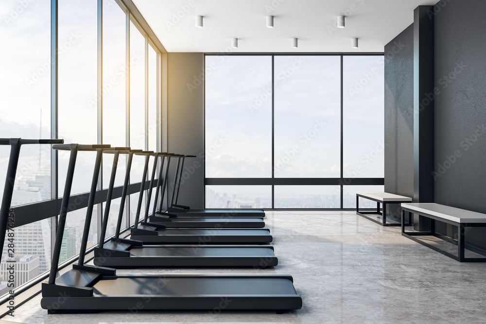 Modern loft style gym with black treadmiils and city view.