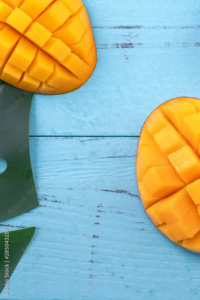 Fresh mango - beautiful chopped fruit with green leaves on bright blue timber background. Tropical f