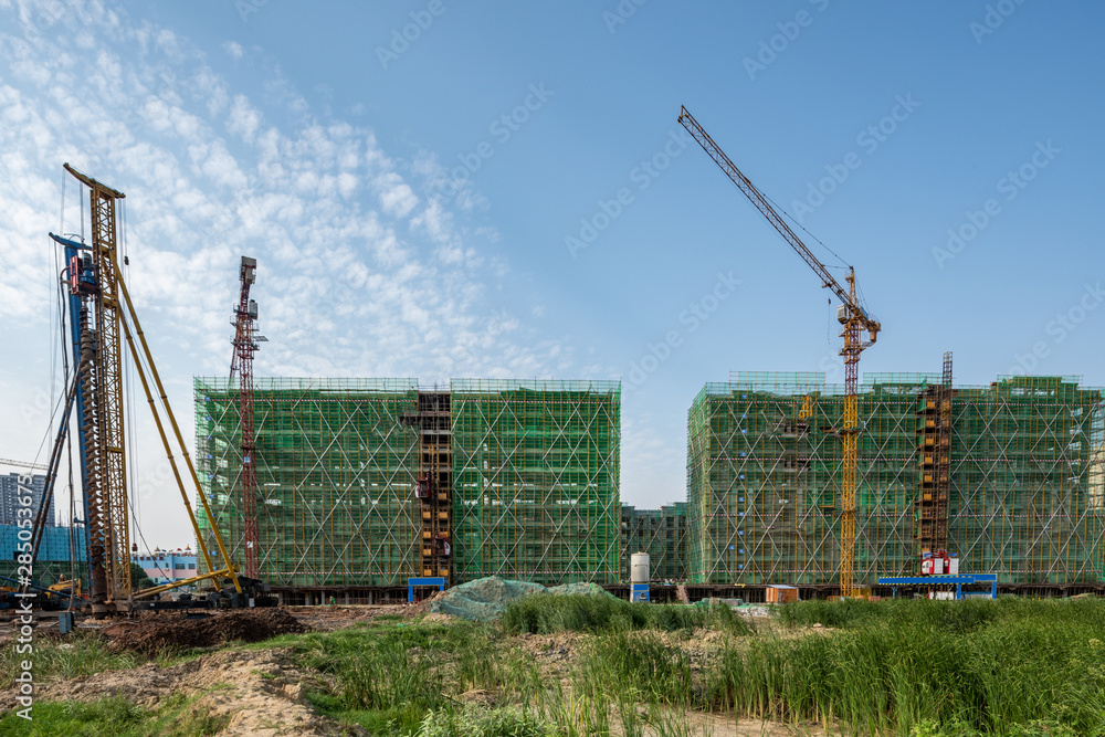 蓝天下的建筑工地、钢结构和起重机。