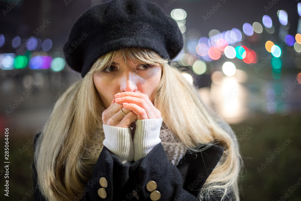 美丽年轻时尚的女人走在夜城的街道上，背景是散焦照明