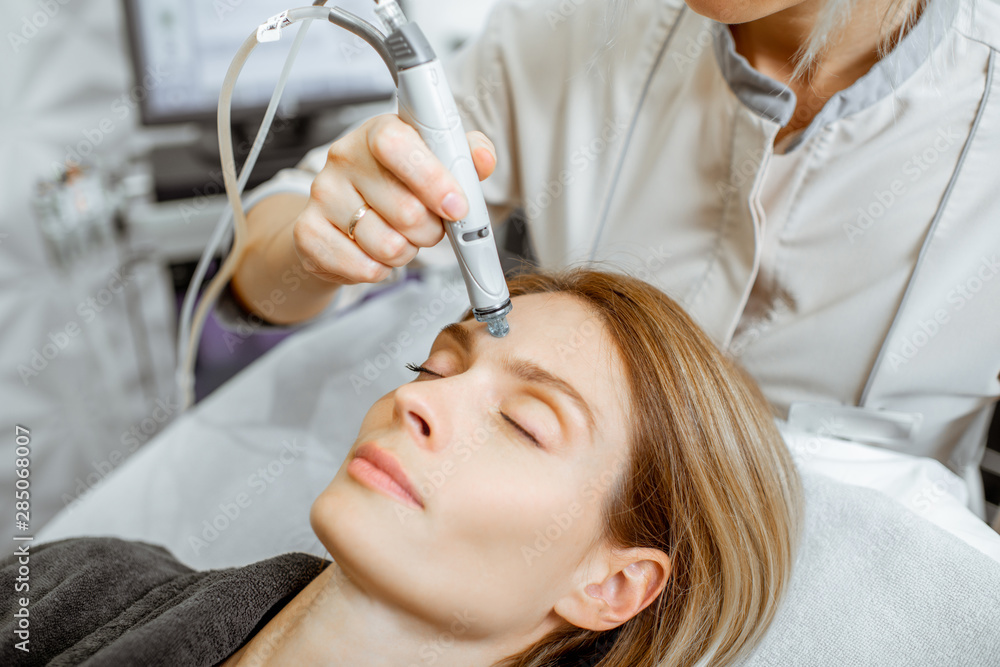 Cosmetologist making vacuum hydro peeling on the forehead region to a woman at the luxury beauty sal