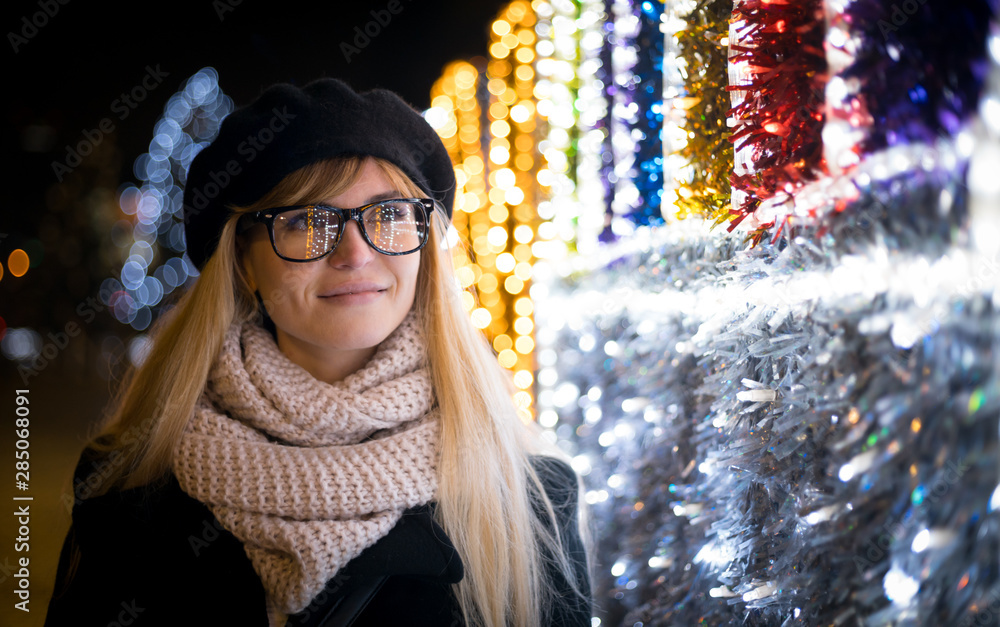 Happy smiling stylish woman walking on illuminated city street during Christmas night