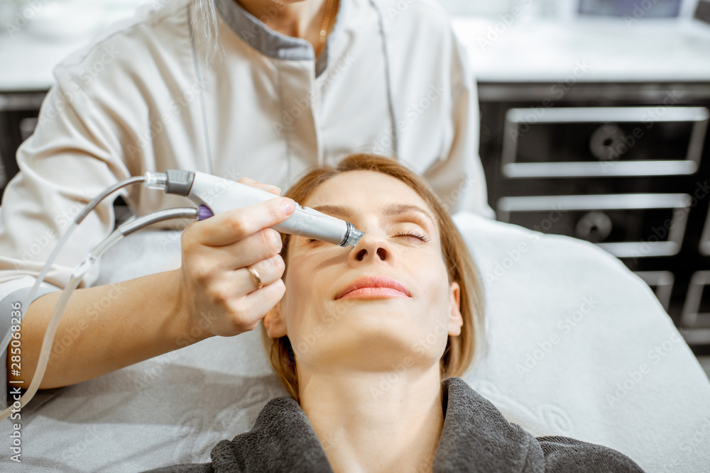 Cosmetologist making vacuum hydro peeling on the nose region to a woman at the luxury beauty salon. 