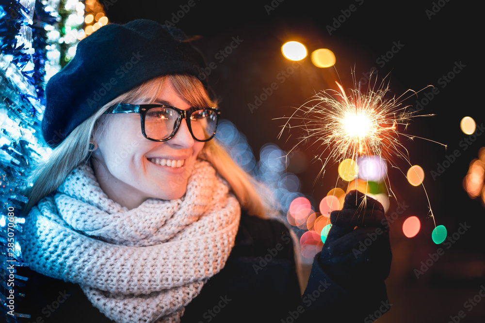 Happy smiling girl holding sparklers standing on illuminated city street during Christmas or New Yea