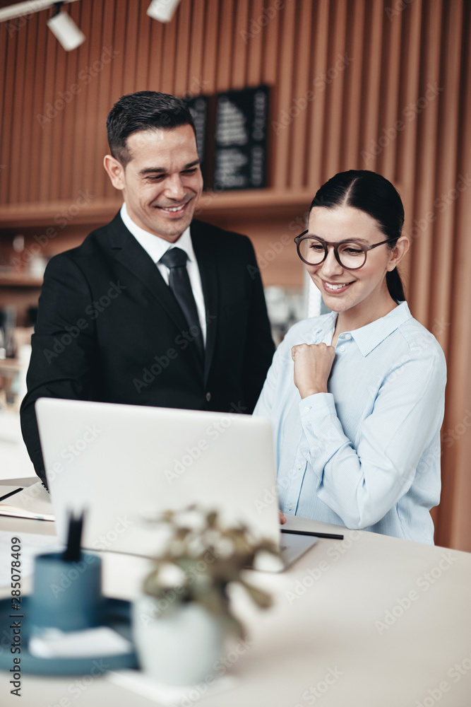 Two smiling businesspeople using a laptop together in an office