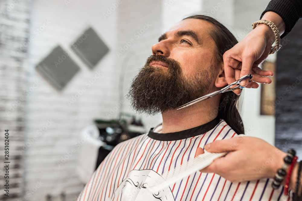 Relaxing at barbershop, close-up cutting beard.