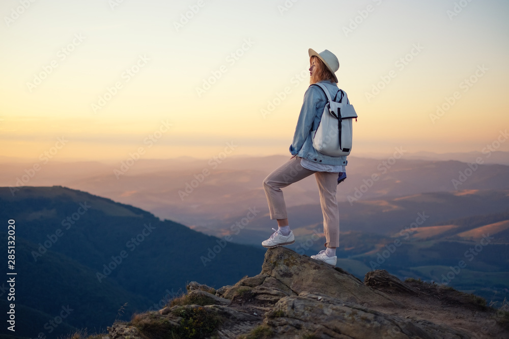 背着背包在山顶徒步旅行。日落时，年轻女孩在山上行走。M