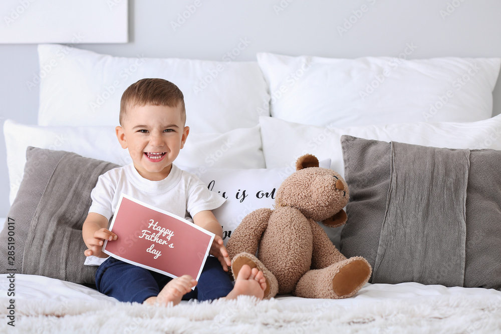 Cute little boy with greeting card for Fathers Day on bed