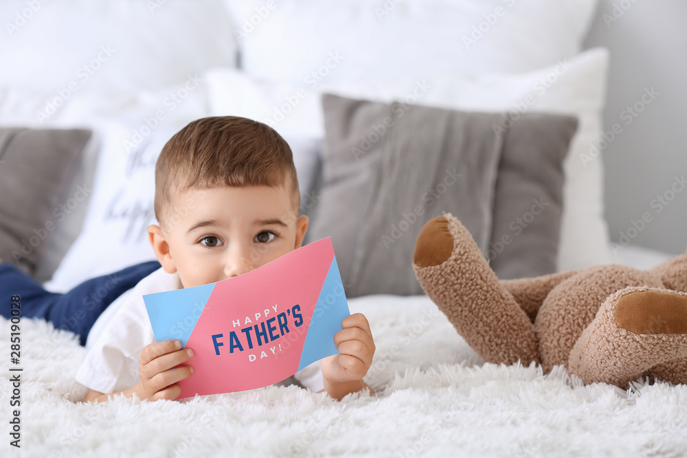 Cute little boy with greeting card for Fathers Day lying on bed