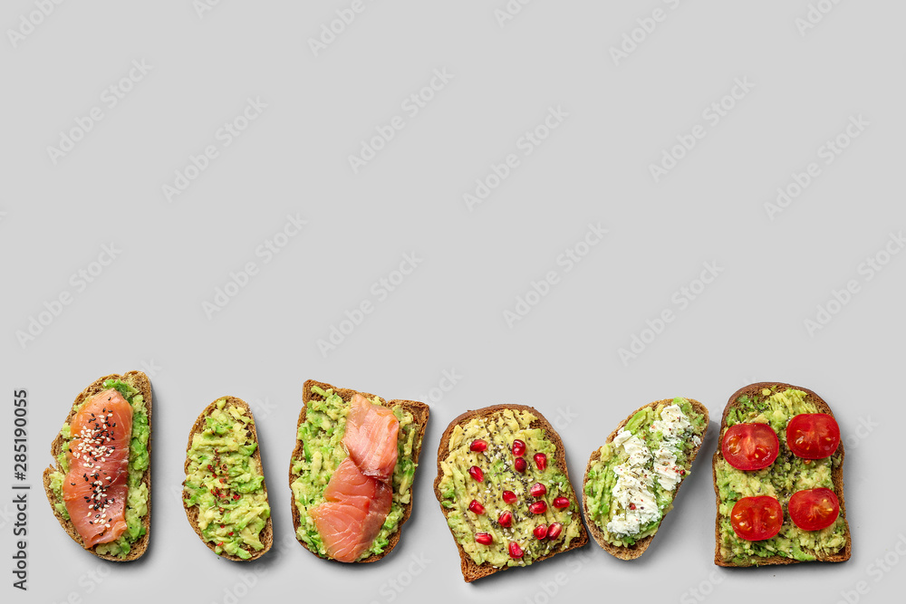 Different tasty avocado toasts on grey background