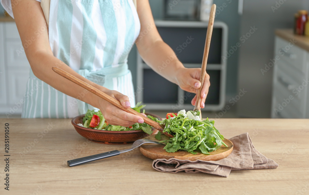 一个女人把美味的芝麻菜沙拉放在厨房桌子上的盘子里