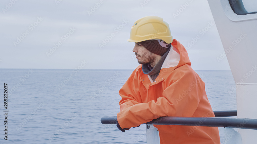 Portrait of Dressed in Bright Protective Coat Fisherman on Commercial Fishing Boat Looking at the Se