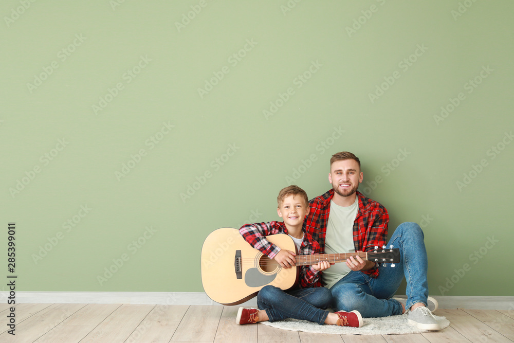 Portrait of happy father and son with guitar sitting near color wall