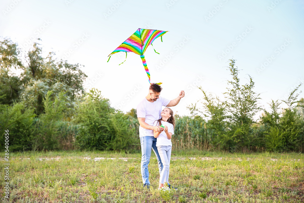 Young man with little daughter flying kite outdoors