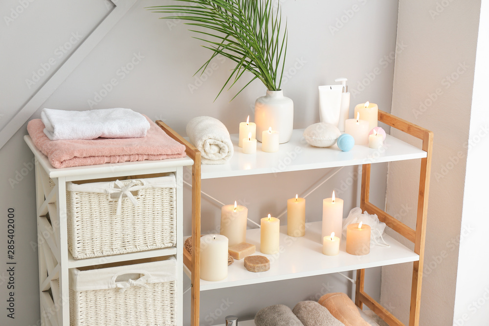 Beautiful burning candles and cosmetics on stand in bathroom