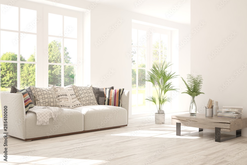 Stylish room in white color with sofa and summer landscape in window. Scandinavian interior design. 