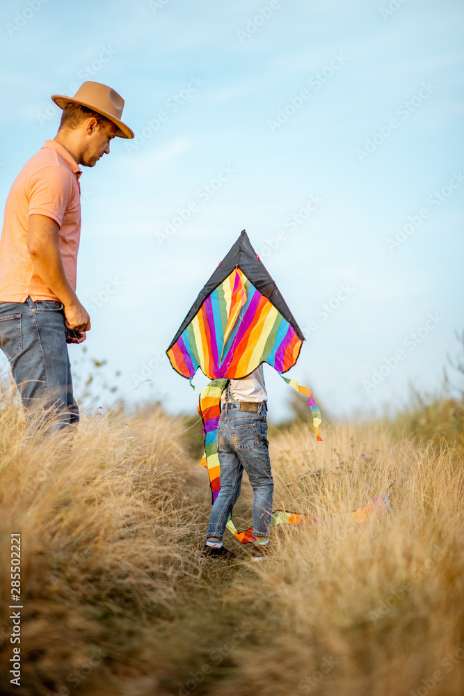 Father with son launching colorful air kite on the field. Concept of a happy family having fun durin