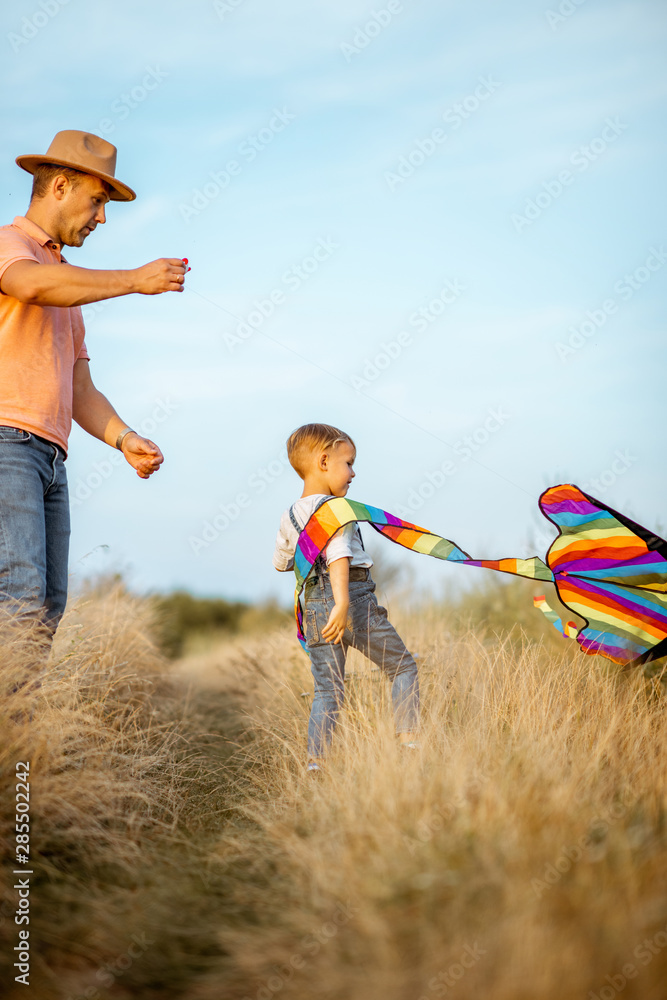 Father with son launching colorful air kite on the field. Concept of a happy family having fun durin