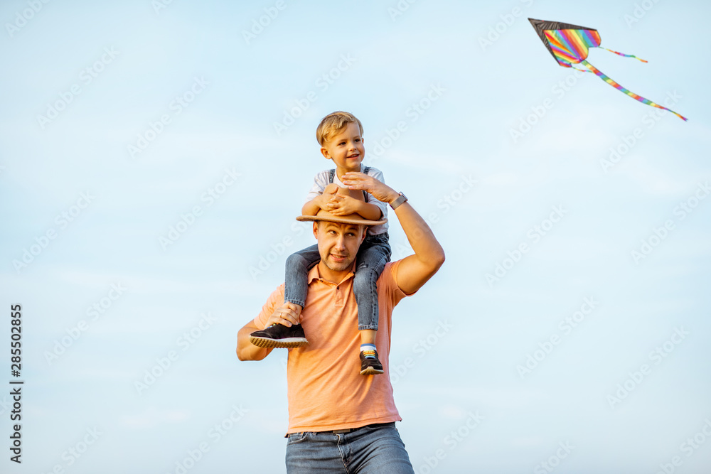 户外蓝天背景下，幸福的父亲和年幼的儿子骑在肩膀上的肖像