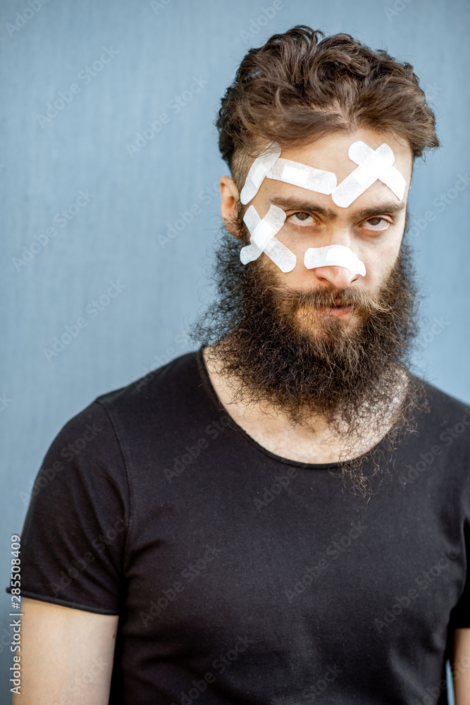 Close-up portrait of an injured man with medical patches on his face on the blue baackground