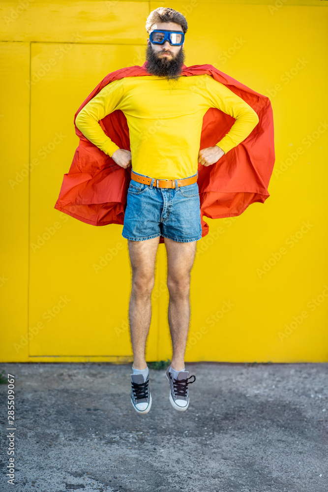 一个像超级英雄一样的男人的肖像，穿着五颜六色的衣服，黄色背景上戴着飞行员眼镜