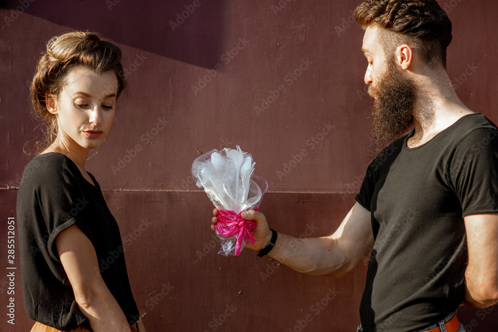 一名男子在深红色背景上向一名年轻女子赠送一束塑料垃圾制成的花束。概念