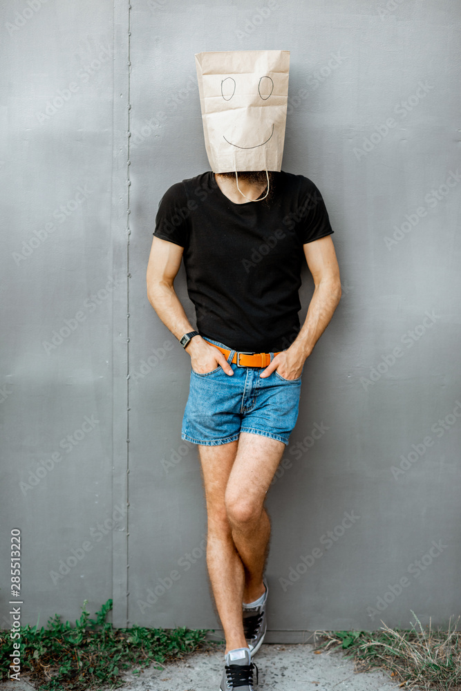 Portrait of a man with paper bag on his head standing on the grey background. Concept of facelessnes