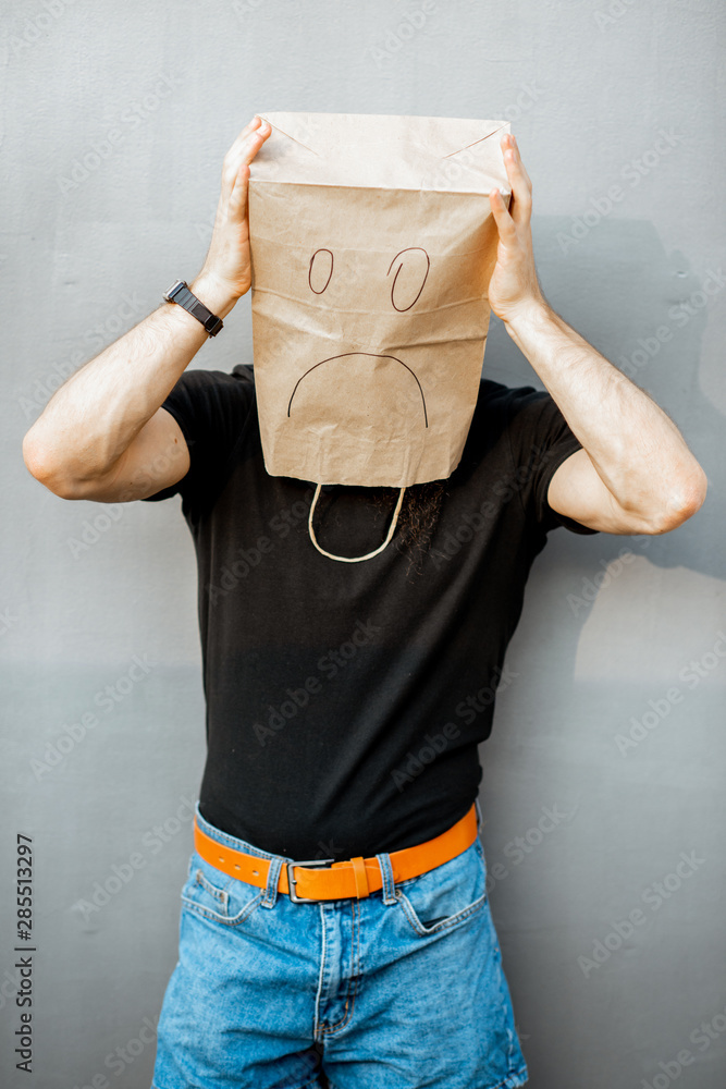 Portrait of a disappointed man with paper bag on his head standing on the grey background. Concept o