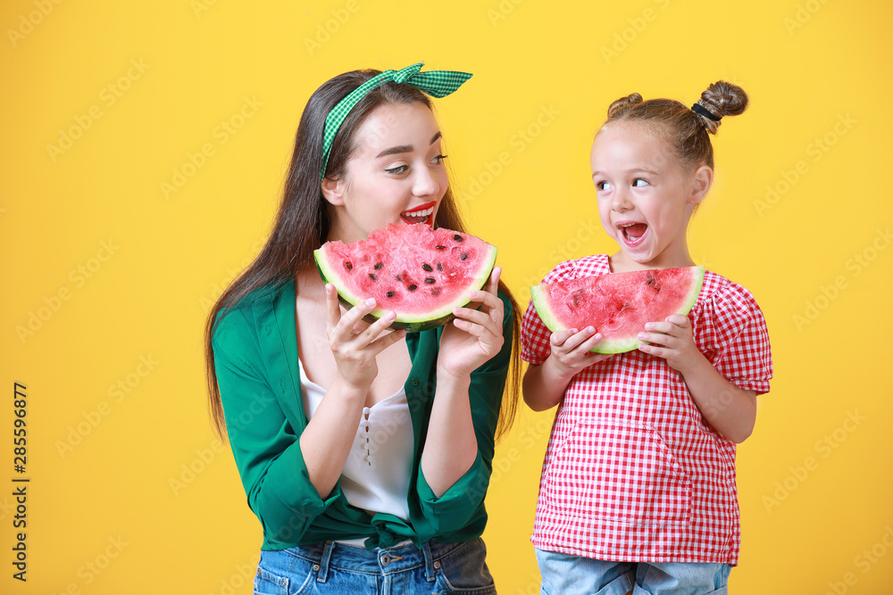 美丽的年轻女子和可爱的女孩，彩色背景上有新鲜的西瓜