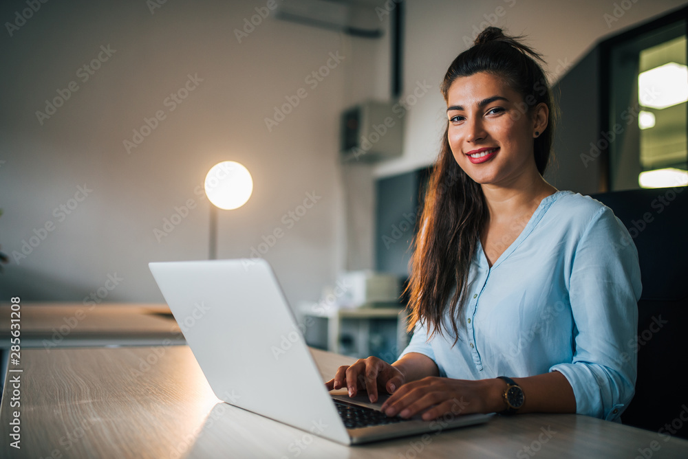 Portrait of a smiling female student with laptop indoors.