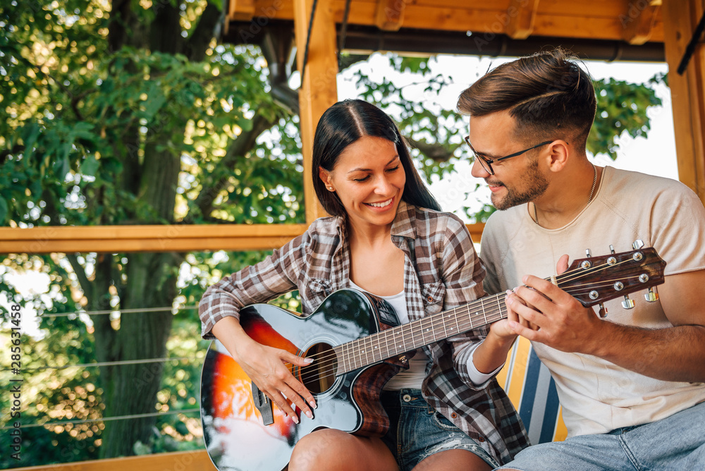 Young woman teaching how to play guitar by a friend.