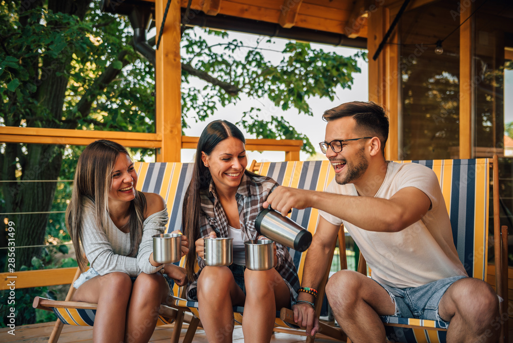 Young people sitting on wooden terrace drinking tea and having fun.