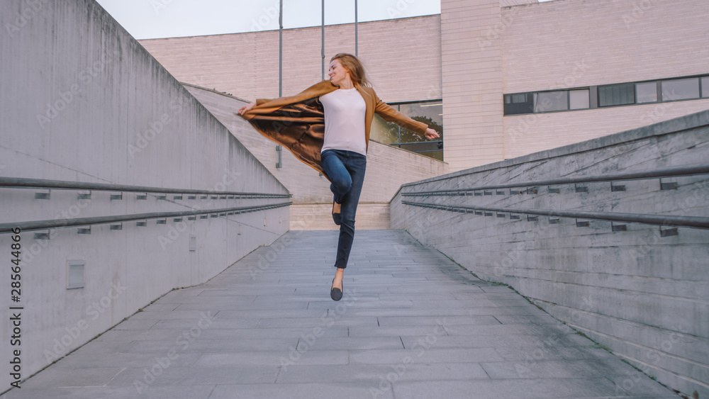 Cheerful and Happy Young Woman Actively Dancing and Jumping While Walking Down a Concrete Urban Path