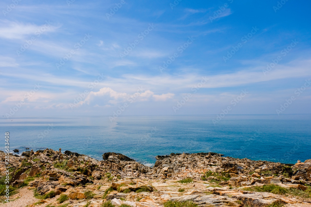 大海地平线，岩石海岸悬崖和阳光蓝色的天空背景。海浪拍打着岩石，