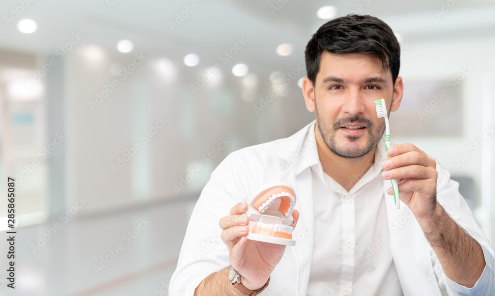 Young male dentist showing toothbrush and denture in dental clinic. Selective focus at the toothbrus