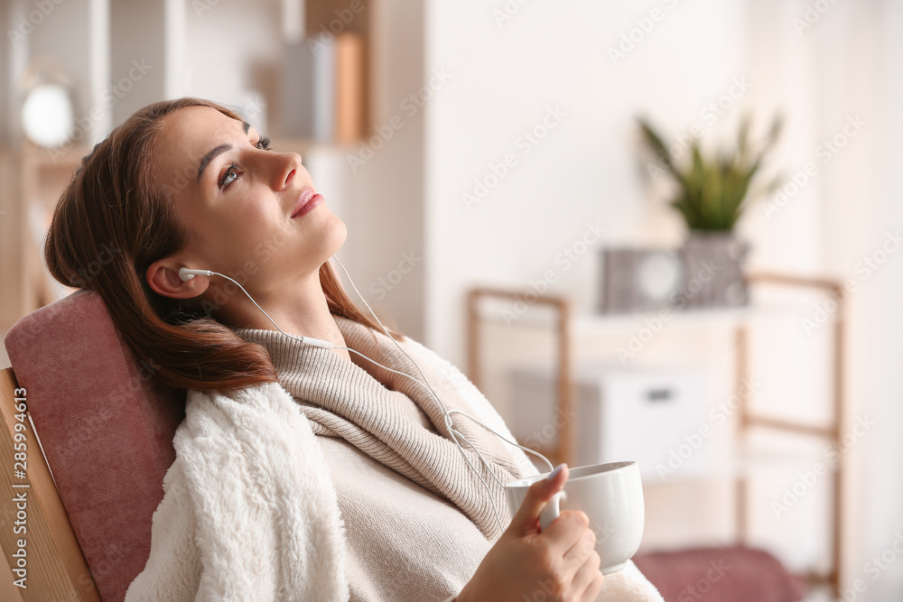 Beautiful young woman drinking tea while listening to music at home