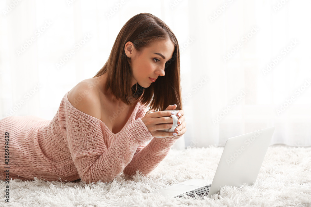 Beautiful young woman with laptop drinking tea at home