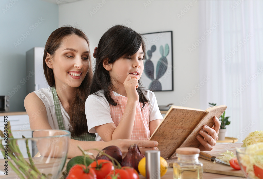 Mother with cute daughter reading cook book in kitchen