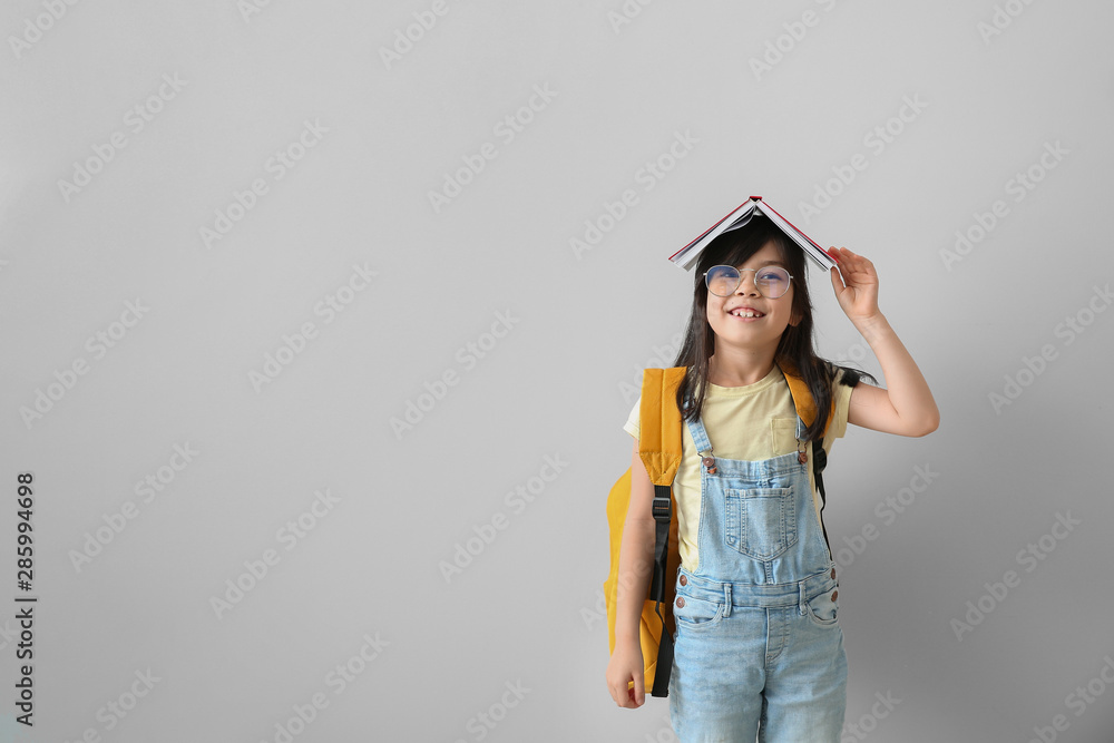 Portrait of happy little schoolgirl with book on light background