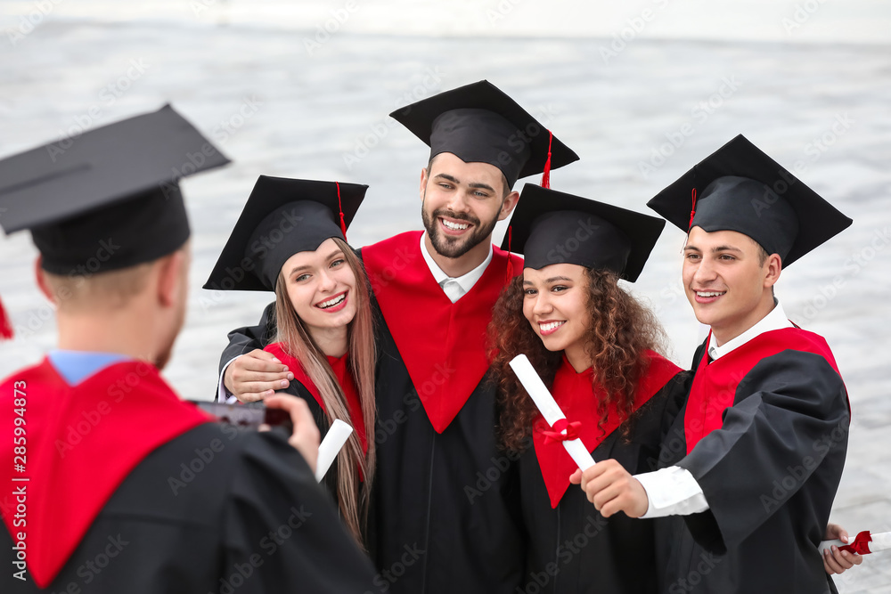 Happy students in bachelor robes and with diplomas outdoors