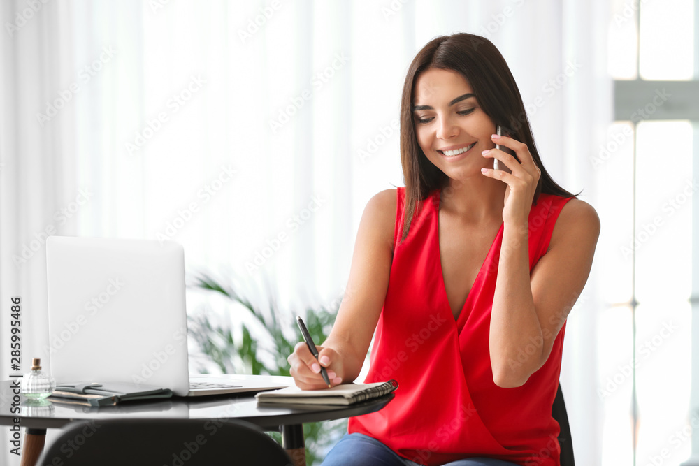 Female blogger with laptop talking by phone in cafe