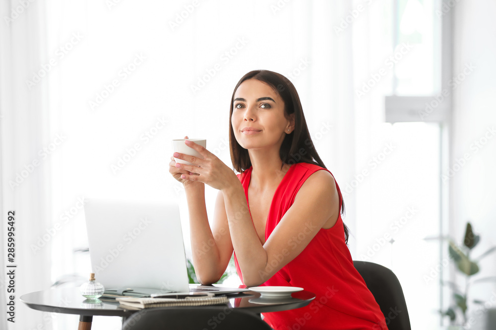 Female blogger with laptop drinking coffee in cafe