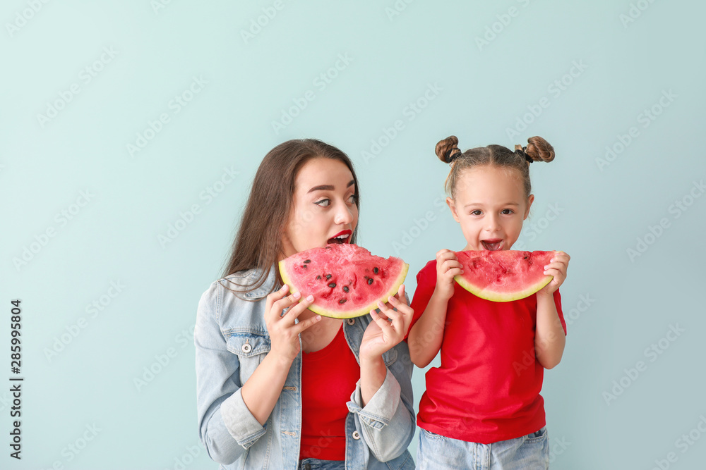 Beautiful young woman and cute girl with fresh watermelon on color background