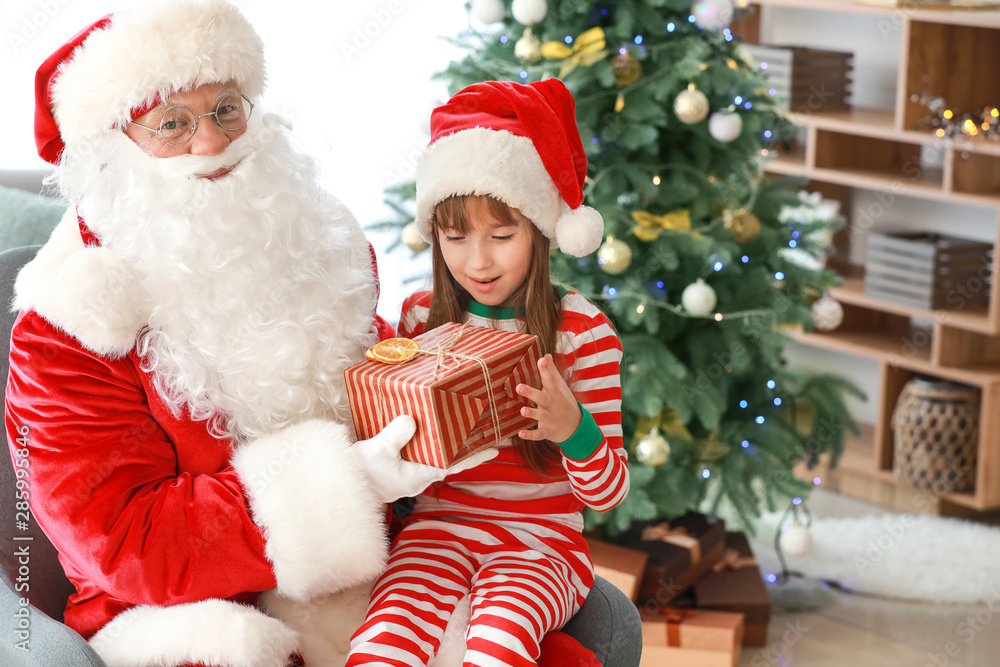 Santa Claus and little girl with gift in room decorated for Christmas