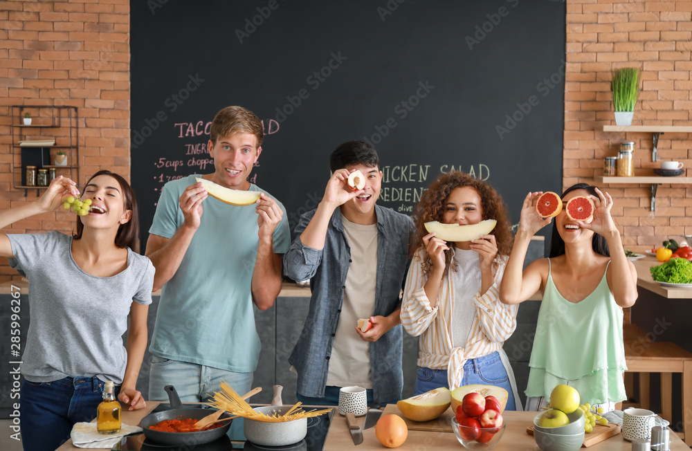 Happy friends having fun with fruits in kitchen