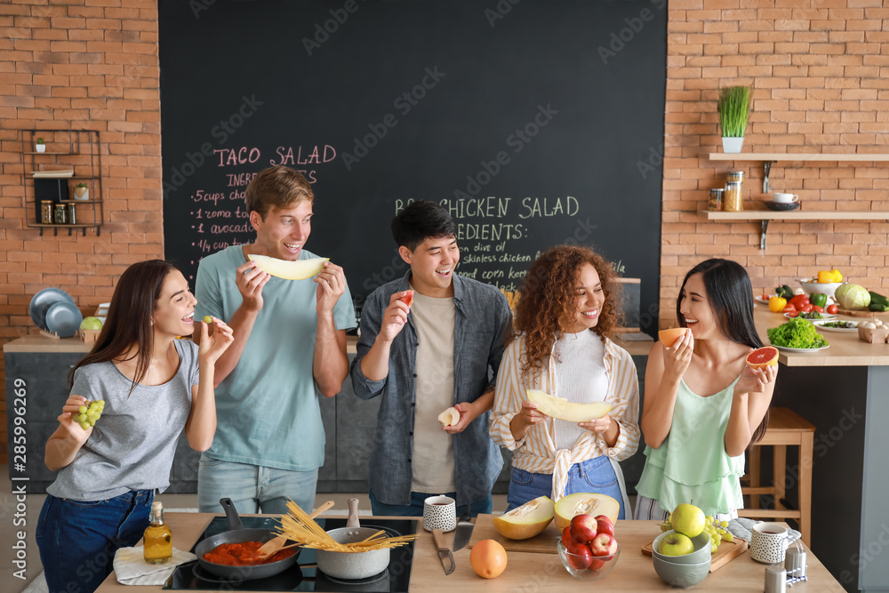 Happy friends eating fruits together in kitchen