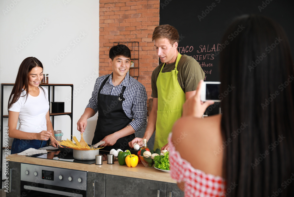 Asian woman taking photo of her friends cooking in kitchen