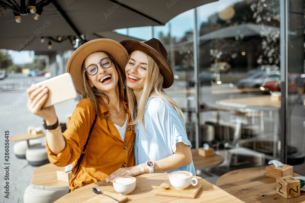 Two female best friends making selfie portrait while spending time together on the cafe terrace duri