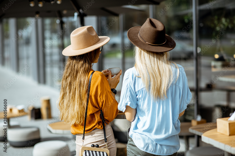 Two girlfriends standing together at the cafe terrace, rear view