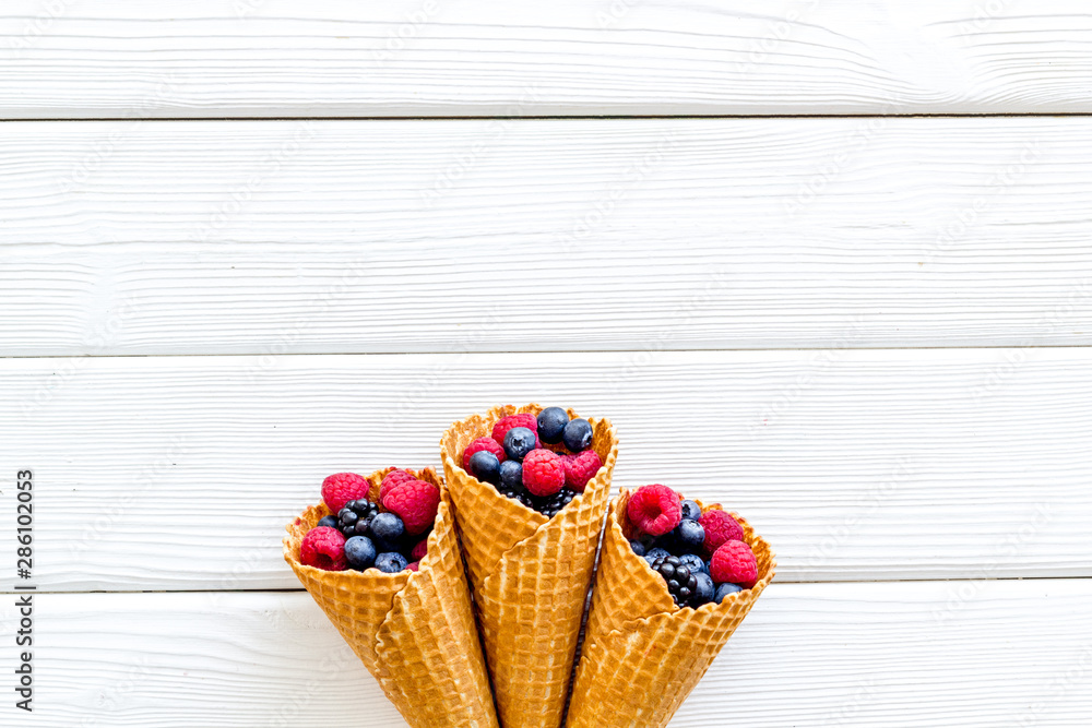 Fresh berries in waffle cones on white wooden background top view mock up